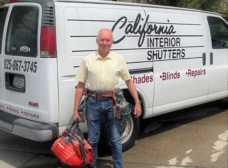 A man wearing a toolbelt carrying a tool bag, standing by the company van